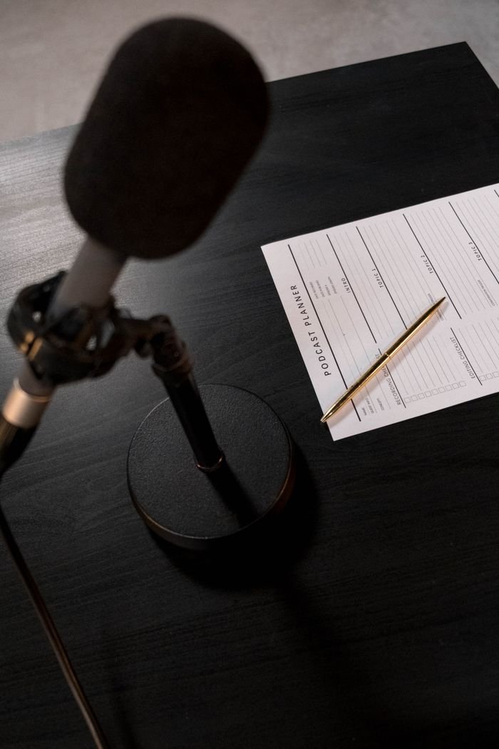 Home A desk setup featuring a microphone and a podcast planning sheet, perfect for audio recording sessions.