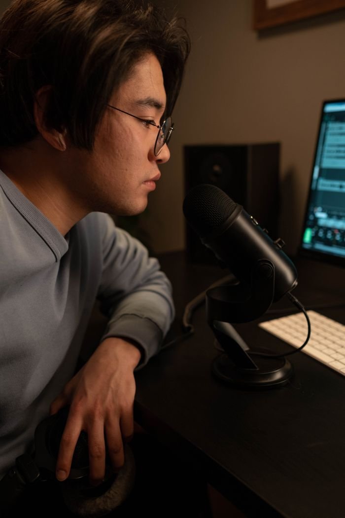 Services Focused young man using a microphone for podcast recording in a dimly lit studio.